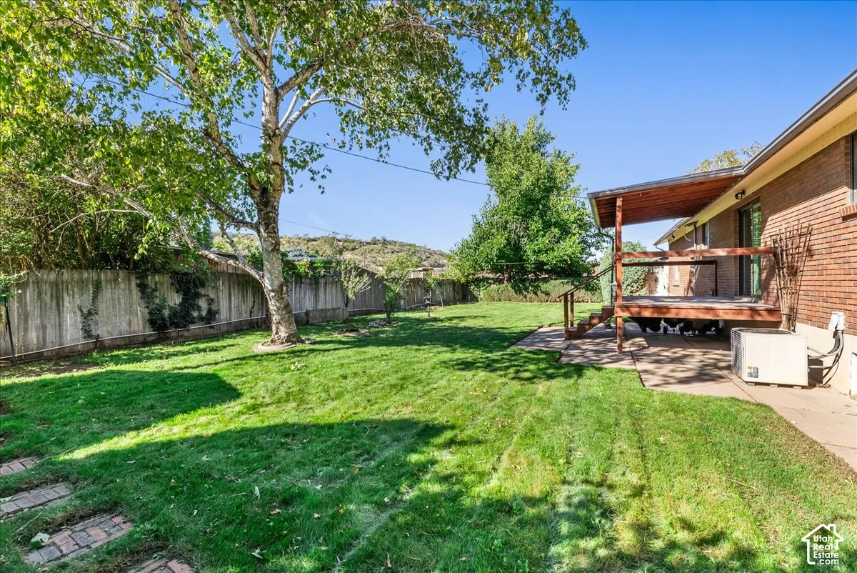 Expansive grassy yard with mature trees, a wood privacy fence, and a covered wood deck