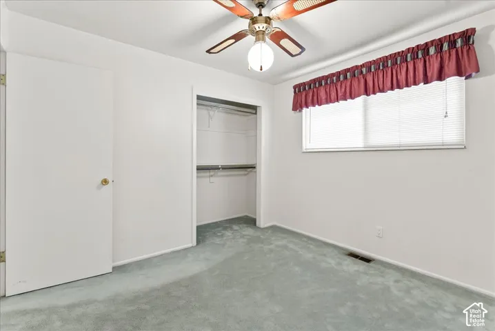 Recessed closet with built-in shelving, ceiling fan with integrated lighting, window with blinds, and light blue carpeting