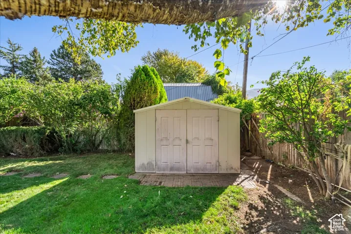 Expansive backyard featuring a manicured lawn, established perimeter landscaping, and a utility shed with double doors on a brick paver foundation