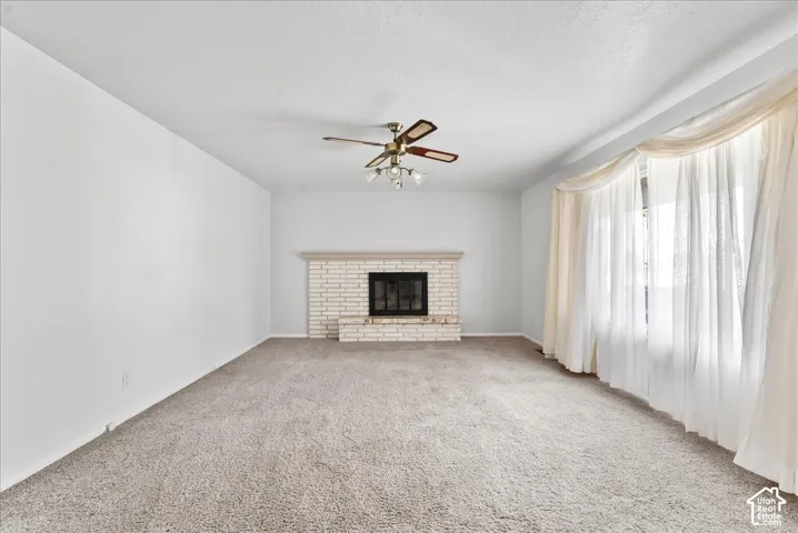 Spacious room featuring a brick fireplace, ceiling fan, and large window with sheer drapes