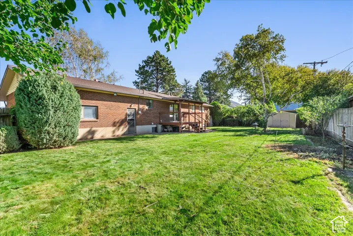 Expansive backyard with a manicured lawn, brick exterior, and a wooden deck