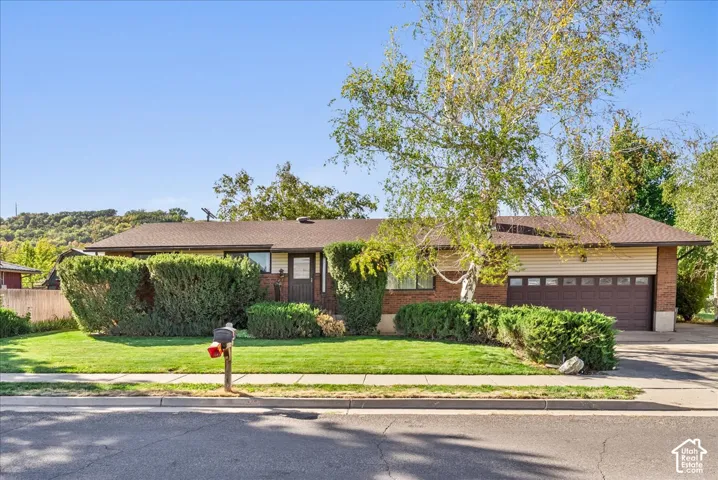 Brick and siding exterior featuring a multi-pane garage door, mature landscaping, and a substantial front lawn