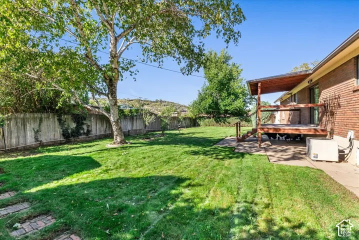 Expansive grassy yard with mature trees, a wood privacy fence, and a covered wood deck