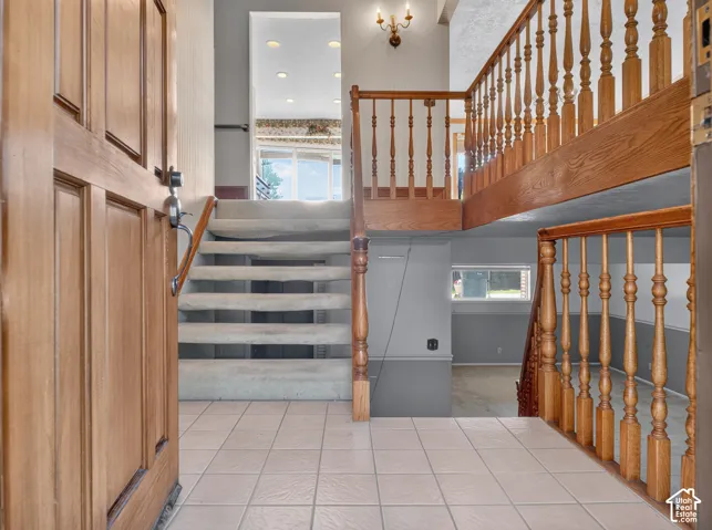 Tile flooring, wood panel front door, wood baluster railing, carpeted staircase, and recessed lighting