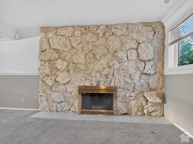 Stone fireplace with a brass-finish insert, tile hearth, and carpeted flooring