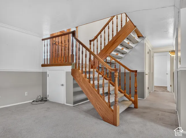 Wooden staircase with turned spindles, light-colored carpeting, two-tone painted walls, and a white interior door