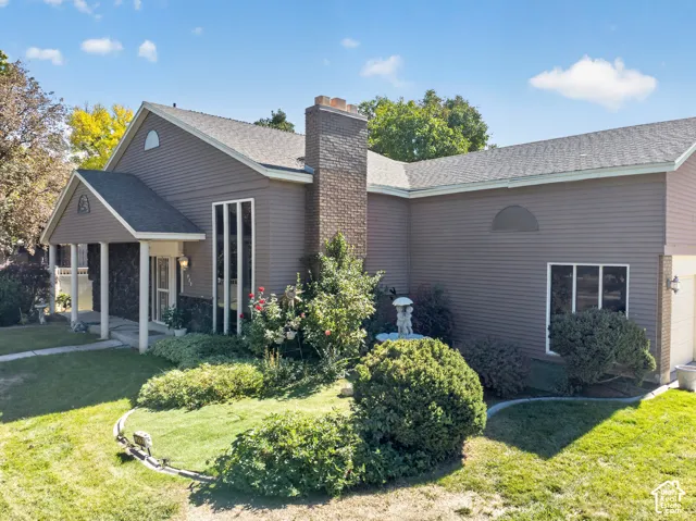 Gable roofline with an arched accent, covered entry porch, dark siding, brick chimney, and mature landscaping