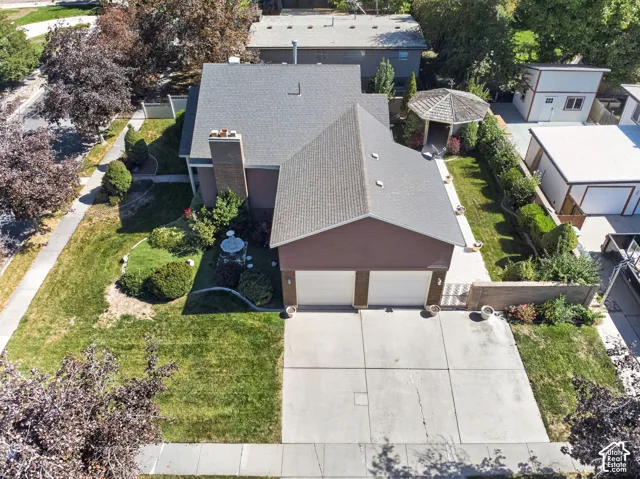 Two-car garage with concrete driveway, mature landscaping, and a side yard with a gazebo