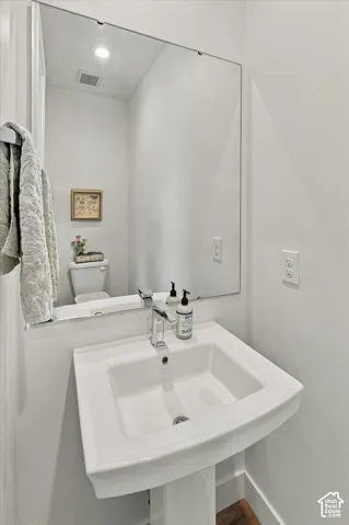 Pedestal sink with a chrome faucet, large frameless wall mirror, and recessed lighting