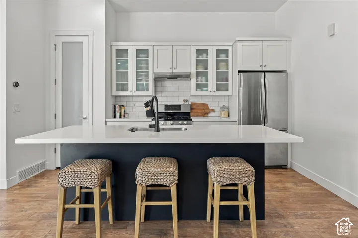 Kitchen featuring a center island with a white countertop, white upper cabinetry with glass inserts, stainless steel appliances, and wood-finish flooring