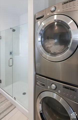 Glass-enclosed shower with a white basin and a stainless steel stacked washer and dryer