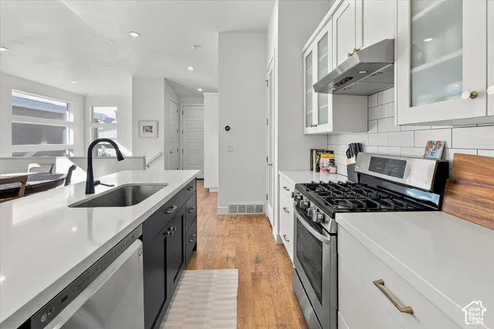 Kitchen featuring light-colored countertops, white subway tile backsplash, stainless steel appliances, and wood-finish flooring