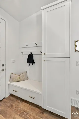 Built-in cabinetry with shaker-style doors, built-in bench seating, storage drawers with brass-finish pulls, wall-mounted coat hooks, and wood-finish flooring