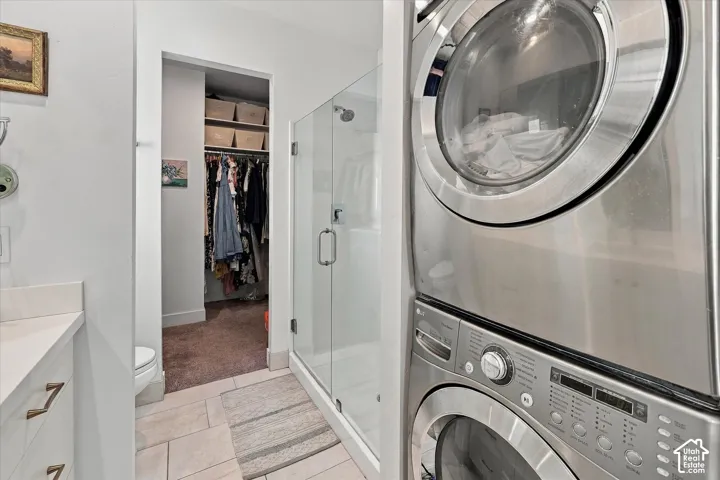 Tiled flooring, glass-enclosed shower, built-in closet shelving, and a built-in stackable washer and dryer