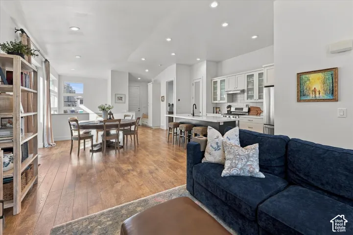 Wood-finish flooring, recessed lighting, white shaker cabinetry, stainless steel appliances, and a kitchen island with seating