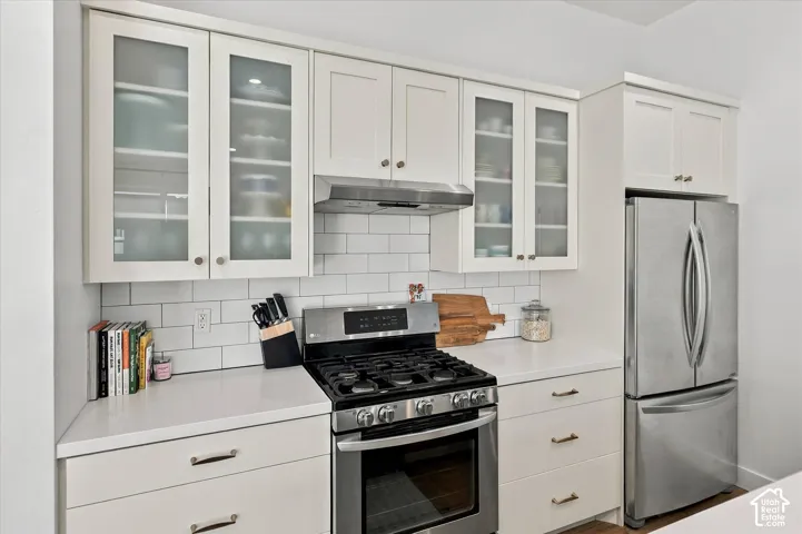 Stainless steel appliances, white subway tile backsplash, white shaker-style cabinetry, frosted glass cabinet doors, and white countertops