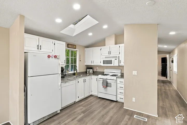 Kitchen featuring white cabinetry, dark countertops, a skylight, recessed lighting, and wood-finish flooring