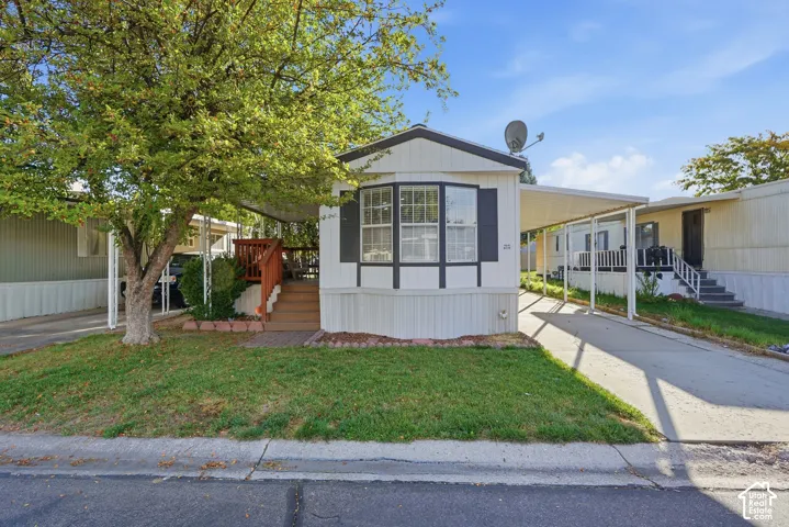 White exterior with dark trim and shutters, covered carport, mature tree, well-maintained lawn, and a porch with wood-finish steps