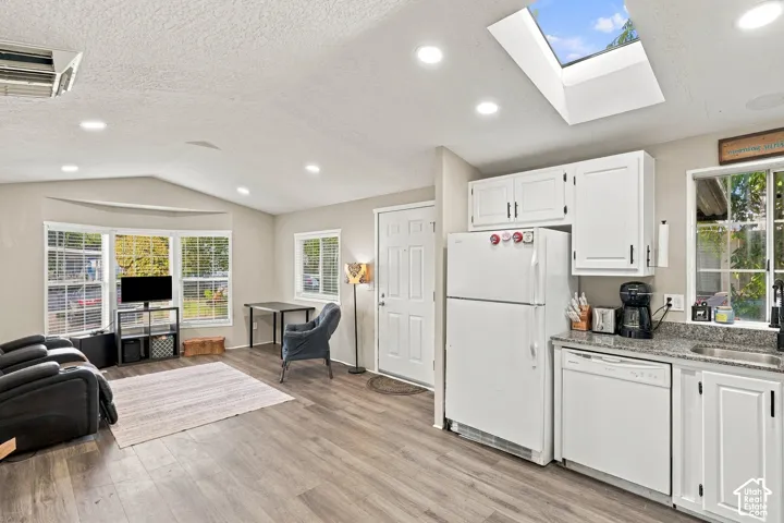 Integrated kitchen and living area featuring wood-finish flooring, a skylight, recessed lighting, white cabinetry, and a bay window