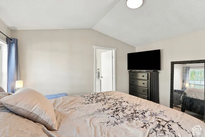 Vaulted ceiling with an overhead light fixture, light-toned wall paint, and a window with curtains