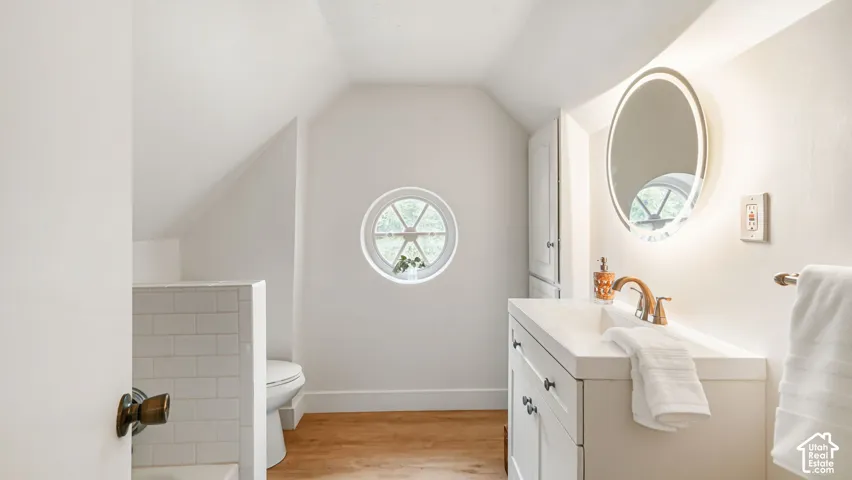 White subway tile shower surround, round window with muntins, wood-finish flooring, white vanity with integrated sink, and illuminated oval mirror