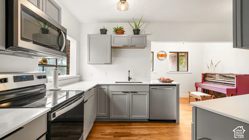 Kitchen featuring stainless steel appliances, light gray cabinetry, light countertops, a stainless steel sink with a black faucet, and wood-finish flooring