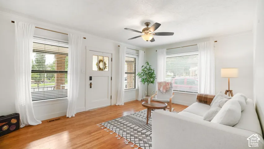 Hardwood-finish flooring, white trim, ceiling fan, multiple windows with blinds, and a paneled entry door with glass inserts