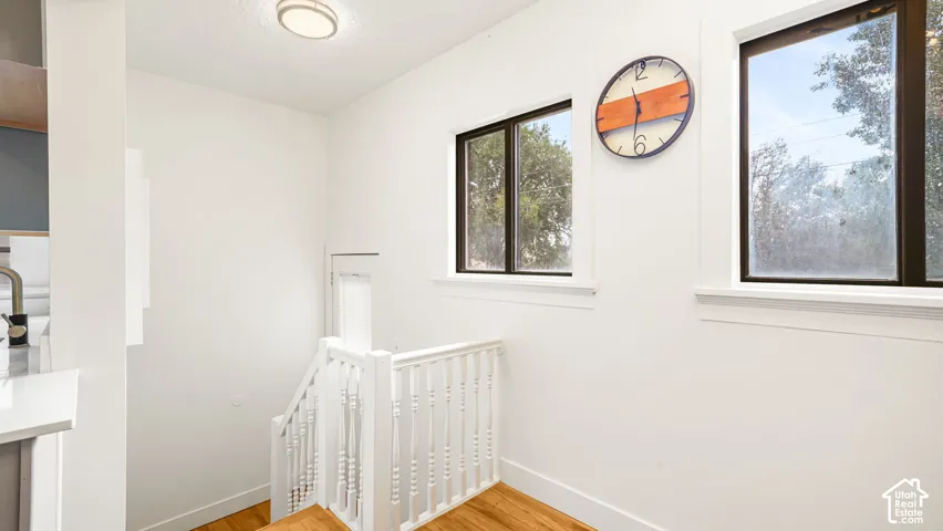 White painted baluster railing, wood-finish flooring, two large windows, white walls, and a ceiling-mounted light fixture