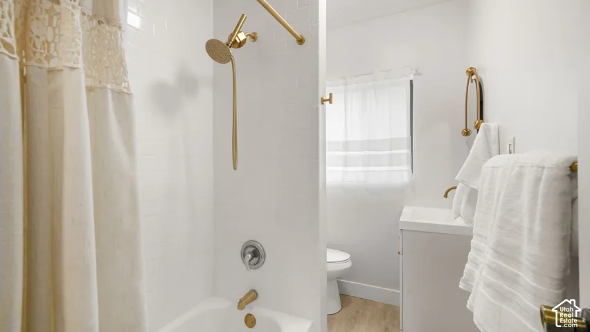 Bathtub with gold-finish shower fixtures, white subway tile surround, white vanity, and wood-finish flooring