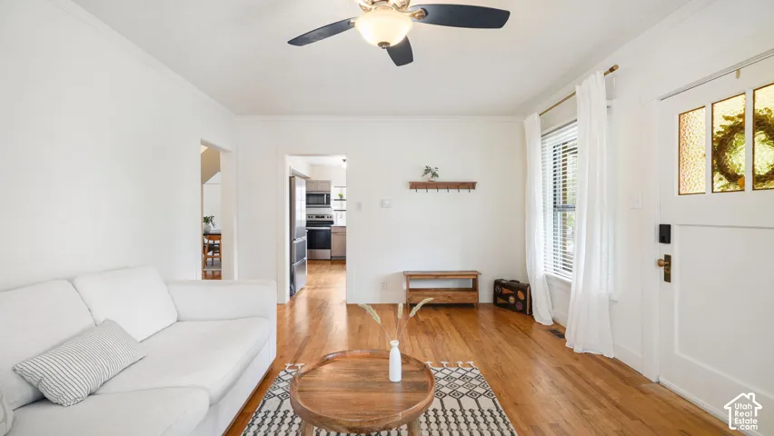 Hardwood flooring throughout, ceiling fan with light fixture, white interior door with stained glass inserts, and a window with blinds