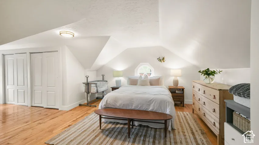 White-painted room with vaulted ceilings, wood-finish flooring, and built-in closet doors