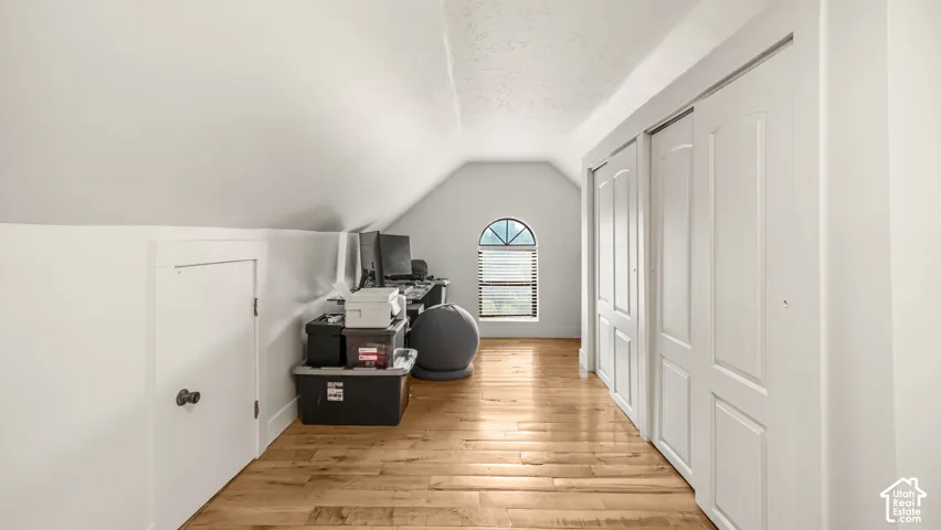Angled ceilings, wood-finish flooring, half-round window with blinds, and white bi-fold closet doors