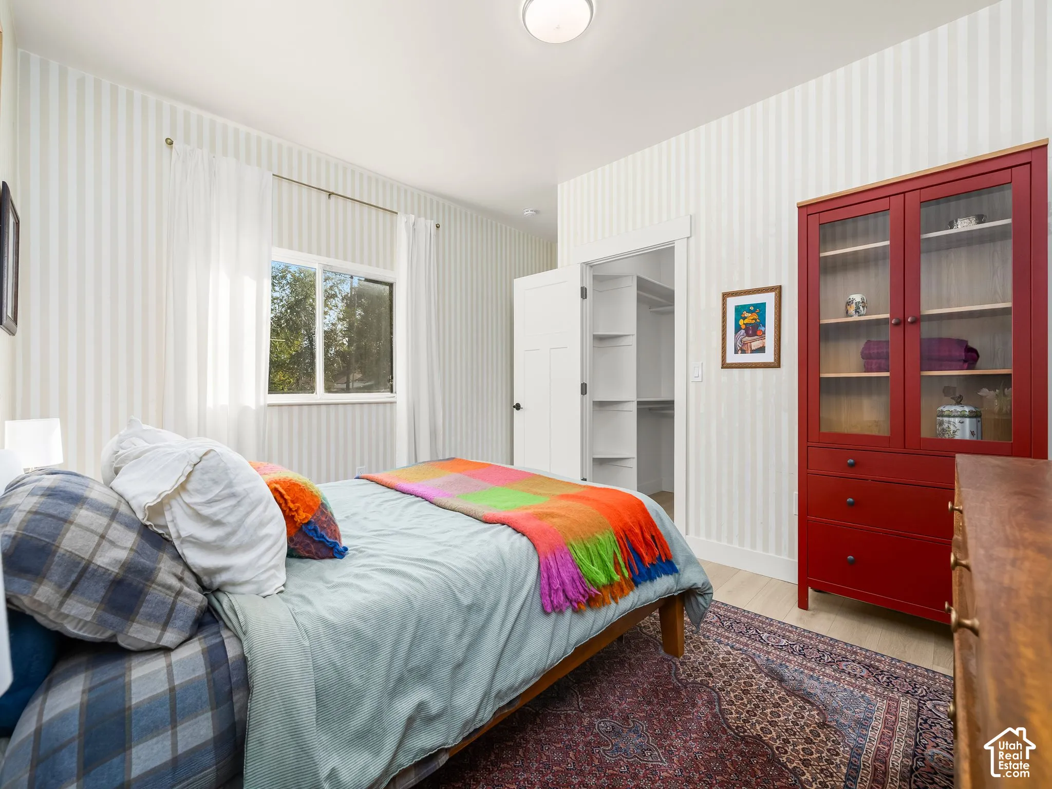 White striped wallpaper, light wood-finish flooring, and a built-in closet with shelving