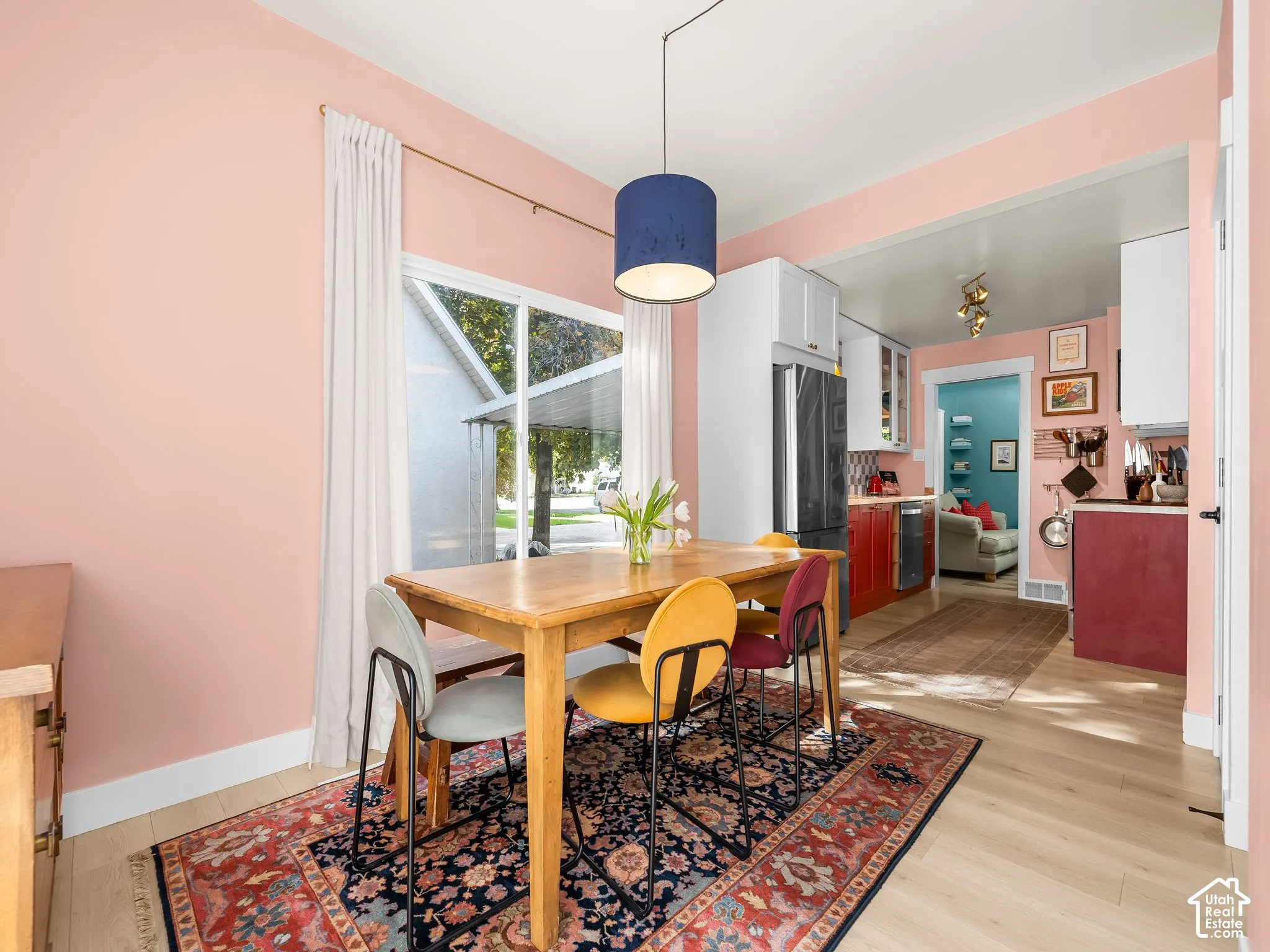 Hardwood-style flooring, large window, overhead lighting fixture, white upper cabinetry, and a black refrigerator