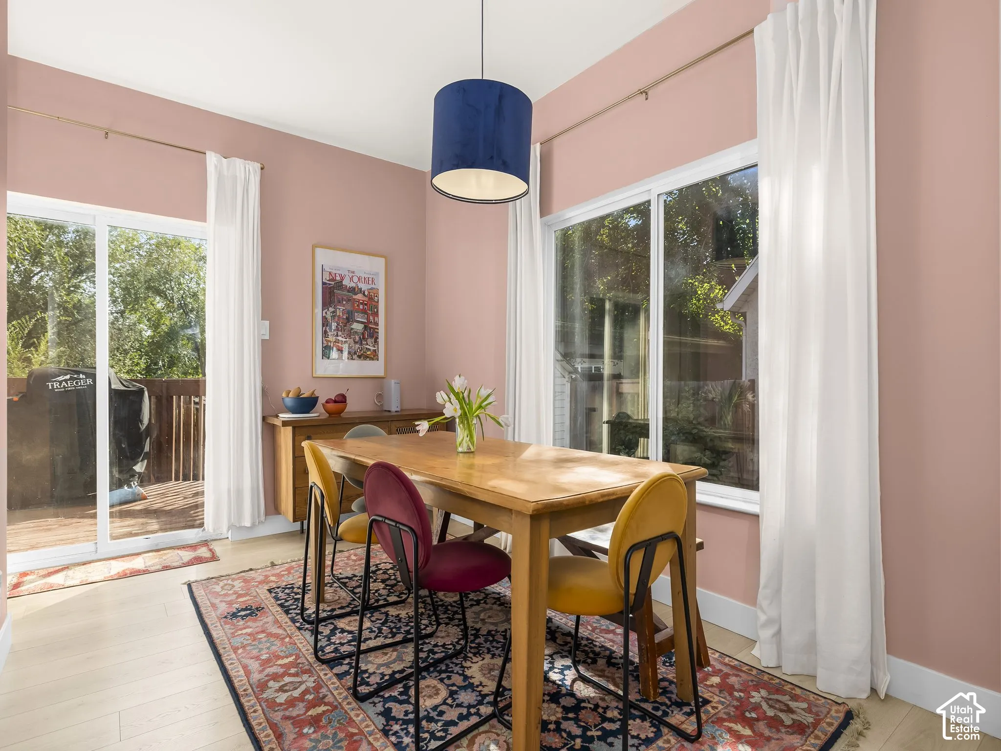Bright dining area showcasing a wood-finish table, pendant lighting with a navy shade, and expansive glass doors and windows framing outdoor scenery