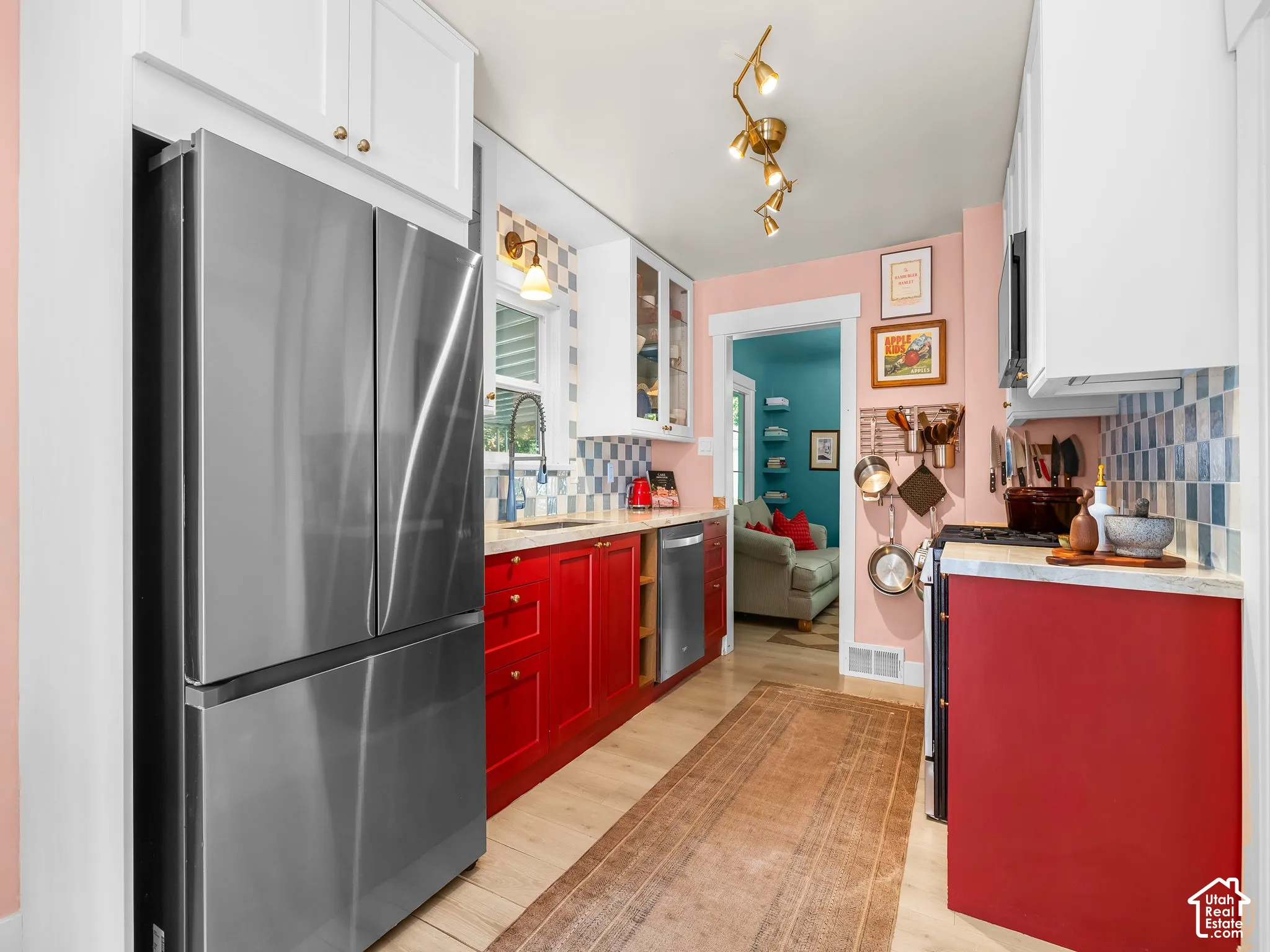 Stainless steel French door refrigerator, wood-finish flooring, white upper cabinetry, red lower cabinetry, and a patterned tile backsplash
