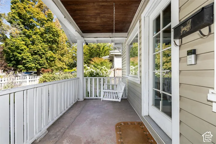 Inviting front porch featuring a wood-finish ceiling, white baluster railing, and a glass-paneled entry door