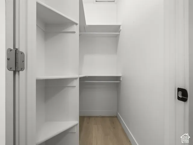 Spacious walk-in closet featuring multiple built-in shelving units with sturdy metal rods for hanging storage, white painted walls, and wood-finish flooring throughout