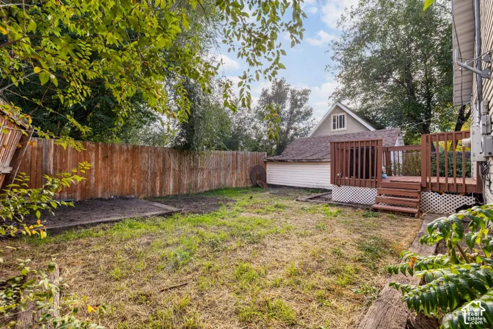 Expansive backyard featuring a wood fence, wood-tone deck with railing, and a detached structure with siding and an A-frame roof