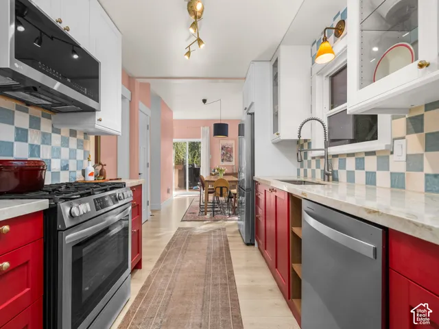 Galley kitchen featuring wood-finish flooring, vibrant red lower cabinetry, white upper cabinetry, and a checkerboard tile backsplash