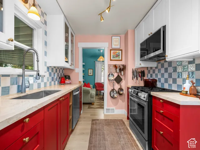 Kitchen featuring red lower cabinetry, white upper cabinetry, a stainless steel sink with a gooseneck faucet, light-toned countertops, and a checkered tile backsplash