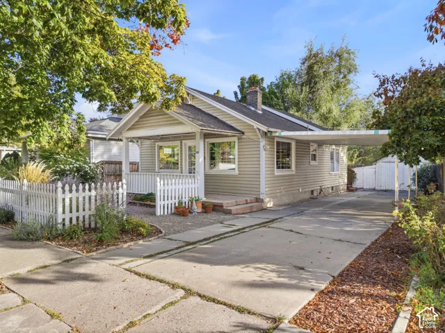 Classic bungalow architecture with a covered front porch, white picket fence, and a long concrete driveway leading to a carport