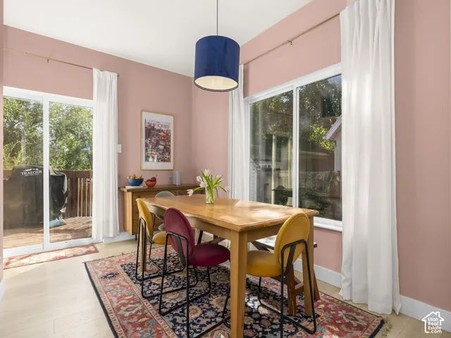 Bright dining area showcasing a wood-finish table, pendant lighting with a navy shade, and expansive glass doors and windows framing outdoor scenery