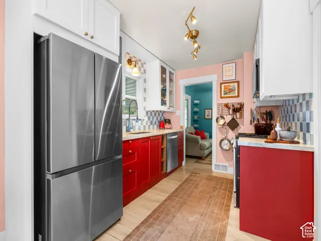 Stainless steel French door refrigerator, wood-finish flooring, white upper cabinetry, red lower cabinetry, and a patterned tile backsplash