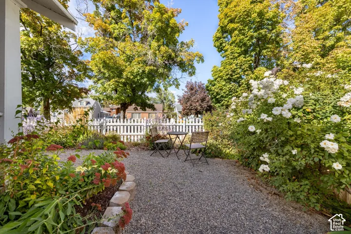 Gravel patio area with a white picket fence, surrounded by mature trees and established landscaping with flowering shrubs