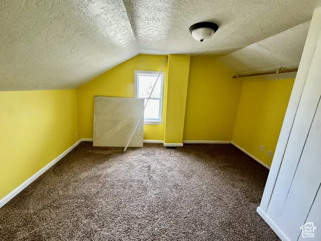 Carpeted room featuring a ceiling-mounted light fixture, window, and sloped ceiling