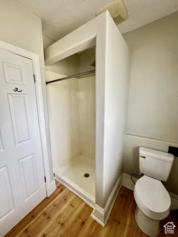 Wood-finish flooring, white panel door, built-in shower stall with white surround, and a white toilet