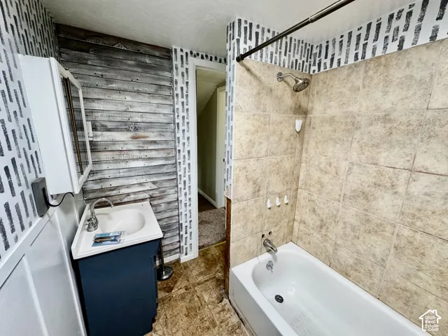 Modern bathroom featuring a floating vanity with integrated sink, tile flooring throughout, and a spacious shower enclosure with stone-finish surround and rainfall showerhead