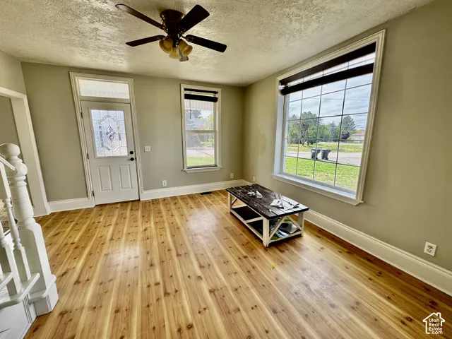 Warm wood-finish flooring, a ceiling fan with integrated lighting, and multiple windows providing natural illumination