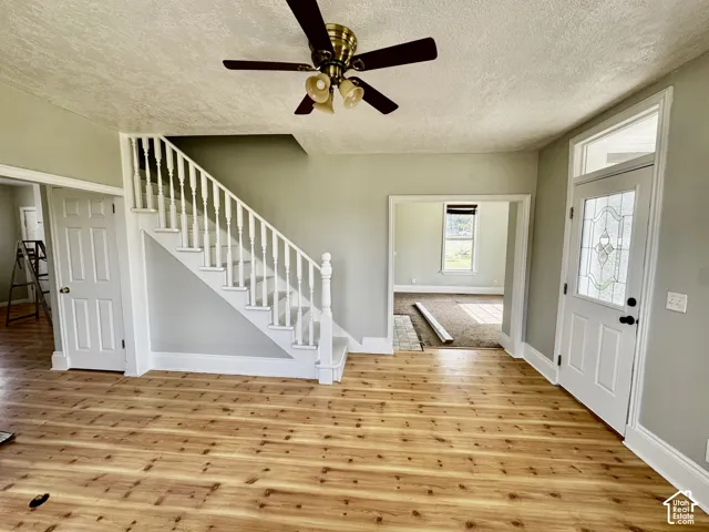 Wood-finish flooring, white staircase with balusters, and a decorative glass entry door with transom window